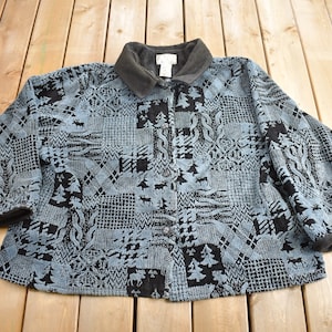 May include: A blue and black patterned fleece jacket with a button-up front and a collar. The jacket has a patchwork design with various patterns, including trees, snowflakes, and geometric shapes.