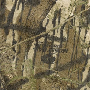 May include: Close-up of a camouflage pattern in shades of brown, green, and tan. The fabric has a textured appearance with the words "MOSS REAL TREE" visible. The design mimics a forest environment.