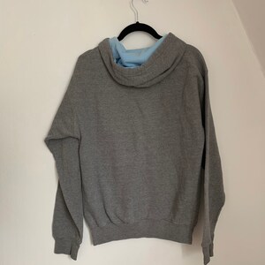 May include: A gray hooded sweatshirt with a light blue lining on the hood. The sweatshirt is hanging on a black hanger.