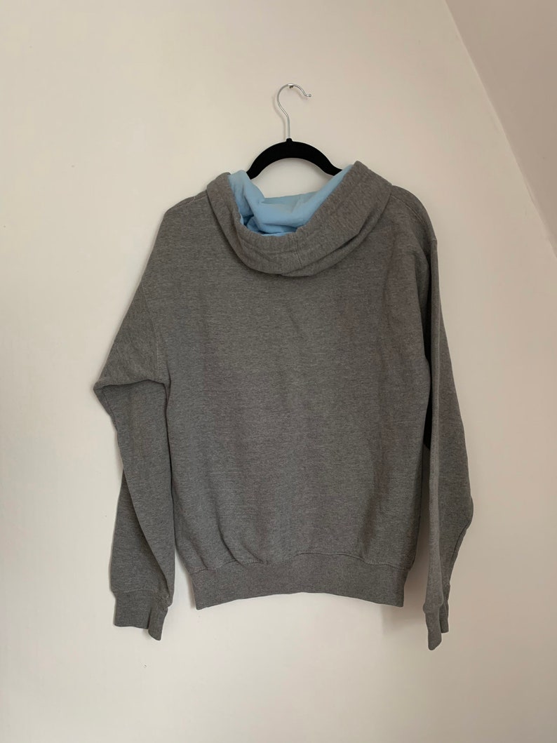 May include: A gray hooded sweatshirt with a light blue lining on the hood. The sweatshirt is hanging on a black hanger.