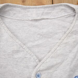 May include: Close-up of the neckline of a gray v-neck shirt with a single button.