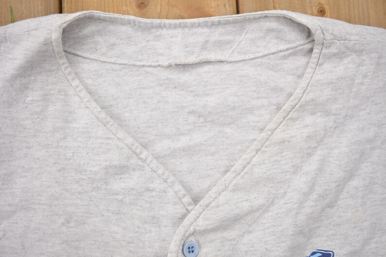 May include: Close-up of the neckline of a gray v-neck shirt with a single button.