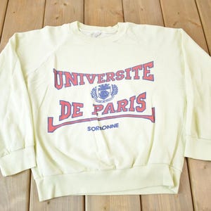 May include: A light yellow sweatshirt with a red and blue print that says "Universite de Paris Sorbonne".