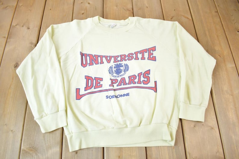 May include: A light yellow sweatshirt with a red and blue print that says "Universite de Paris Sorbonne".