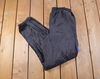 May include: Black nylon track pants with a red and blue stripe down the side.