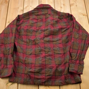 May include: A red and brown plaid flannel shirt with long sleeves and a button-up front.