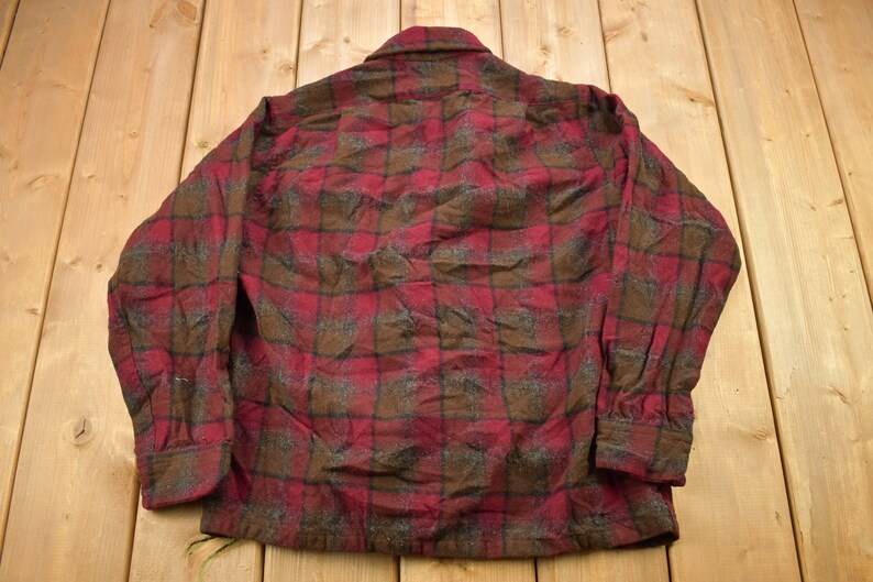 May include: A red and brown plaid flannel shirt with long sleeves and a button-up front.