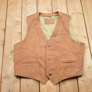 May include: A brown leather vest with a V-neck and four buttons. The vest has two pockets on the front.