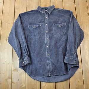May include: A long-sleeved, dark blue corduroy shirt with a button-down collar and two chest pockets.