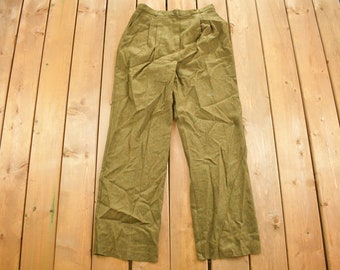 Könnte beinhalten: Eine olivgrüne Hose mit Falten an der Vorderseite. Die Hose ist aus einem strukturierten Stoff und hat eine lockere Passform.