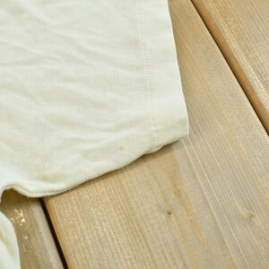 May include: A plain, off-white short-sleeved t-shirt made of a soft, lightweight fabric. The garment features a simple crew neckline and a standard hemmed sleeve, showcasing a clean, solid-colored design with a subtle, light texture throughout.