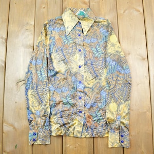 May include: A long-sleeved shirt with a yellow, blue, and brown floral pattern. The shirt has a collar and a button-up front.