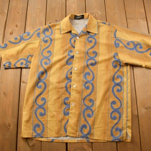 May include: A yellow short-sleeved button-down shirt with a blue and yellow patterned design.