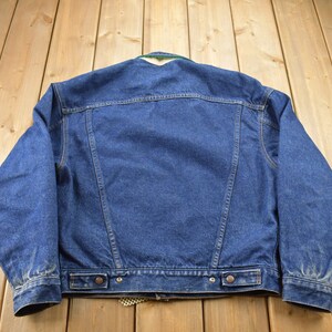 May include: A blue denim jacket with a green and white plaid lining. The jacket has a button closure and two pockets on the front.