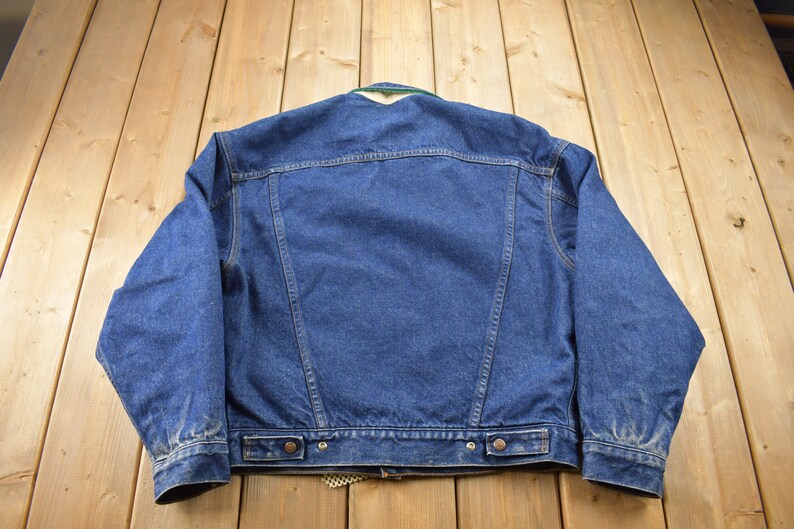 May include: A blue denim jacket with a green and white plaid lining. The jacket has a button closure and two pockets on the front.