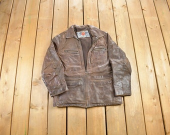 May include: A brown leather jacket with a zipper closure and multiple pockets. The jacket has a label that reads "Rampage" in white letters on a red background.