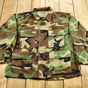 May include: A camouflage-patterned jacket with multiple pockets. The jacket is made of a durable fabric and has a button-up closure.