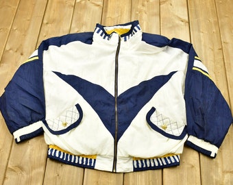 May include: A white, blue, and yellow windbreaker jacket with a zipper closure. The jacket has a V-shaped design on the front and a striped band around the bottom.