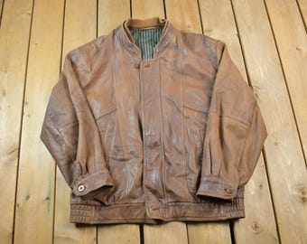 May include: A brown leather bomber jacket with a zipper closure and a ribbed collar. The jacket has a striped lining and two pockets on the front.