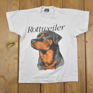 May include: White t-shirt with a black and brown Rottweiler dog graphic and the text "Rottweiler" printed on the front.