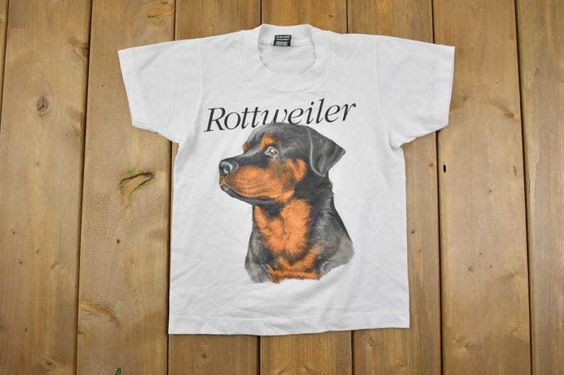 May include: White t-shirt with a black and brown Rottweiler dog graphic and the text "Rottweiler" printed on the front.