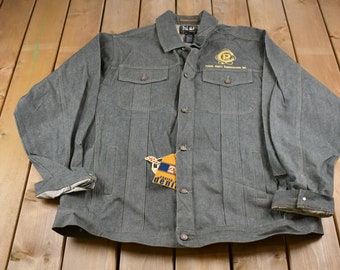 Puede incluir: Una chaqueta vaquera gris con una etiqueta amarilla y azul que dice "Carter Denim". La chaqueta tiene un bolsillo en el pecho izquierdo con un logotipo bordado que dice "Prime Roll Entertainment Inc."