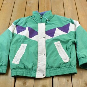 May include: A green, white, and purple color block jacket with a zipper closure and a drawstring waist.