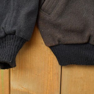 May include: Two jacket sleeves made of a thick, textured fabric. The left sleeve is black with a ribbed black knit cuff, while the right sleeve is dark brown with a matching ribbed black knit cuff. Both sleeves feature a visible seam detail.