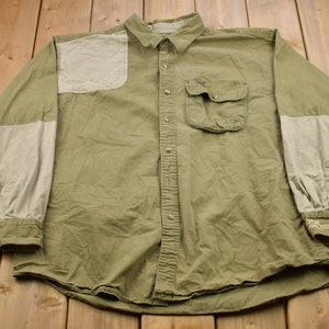 May include: A green long-sleeved button-up shirt with beige patches on the shoulders and sleeves. The shirt has a single chest pocket and a button-down collar.