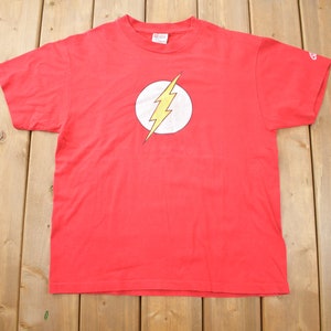Puede incluir: Camiseta roja con un gráfico de rayo amarillo en un círculo blanco. El gráfico es el logotipo de Flash.