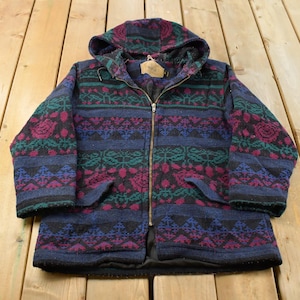 May include: A long-sleeved hooded jacket featuring a full-length front zip and two front pockets. The garment is decorated with a repeating geometric and floral pattern in shades of dark blue, magenta, and teal throughout the fabric.