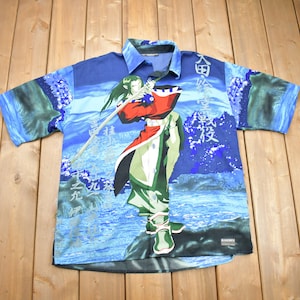 May include: A blue, short-sleeved button-down shirt with a colorful anime character print. The character is holding a sword and is surrounded by water and clouds. The shirt has Japanese text on it.