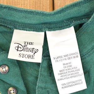 May include: Green Henley shirt from The Disney Store, featuring a button-down placket and a graphic of a cartoon character. The shirt has a tag that reads "X-Large". Made of 100% cotton.