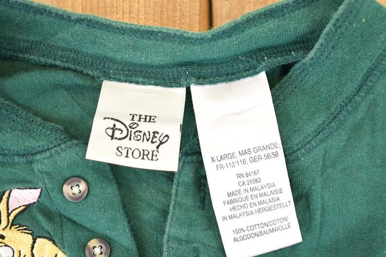 May include: Green Henley shirt from The Disney Store, featuring a button-down placket and a graphic of a cartoon character. The shirt has a tag that reads "X-Large". Made of 100% cotton.