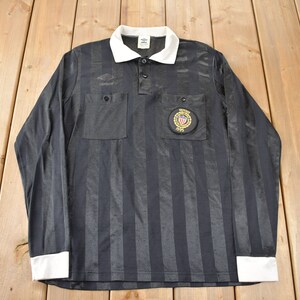 May include: Black and white striped referee shirt with long sleeves and a white collar. The shirt has a patch on the chest with the text "National Association of Sports Officials" and the letters "NASO".