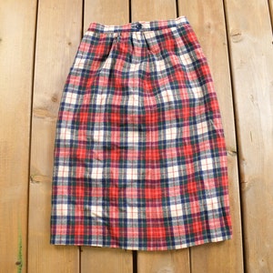 May include: A red, white and blue plaid skirt with a button fastening. The skirt is made from a thick, woven fabric.