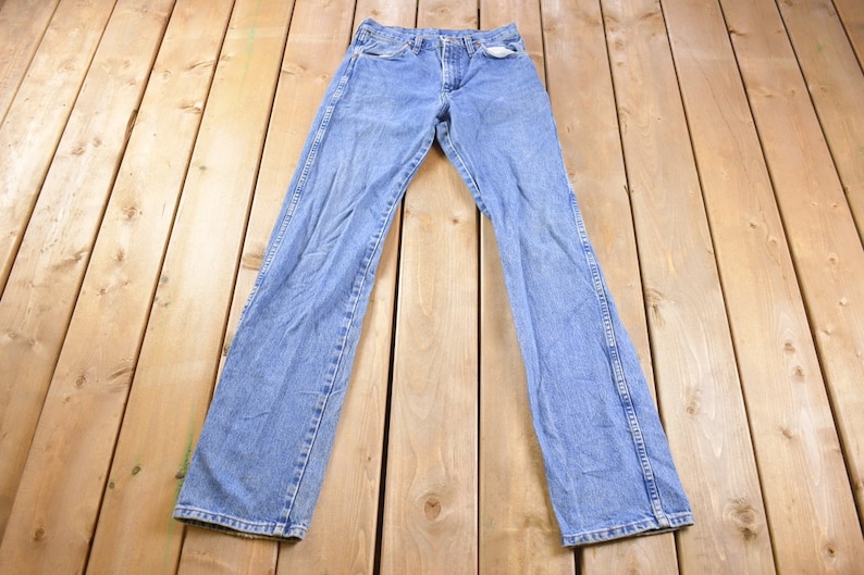 May include: A pair of light blue denim jeans laid flat on a wooden surface.