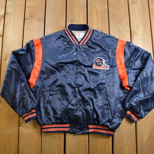 May include: A navy blue satin bomber jacket with orange and white striped trim. The jacket has a button closure and a large "Bears" logo on the front.