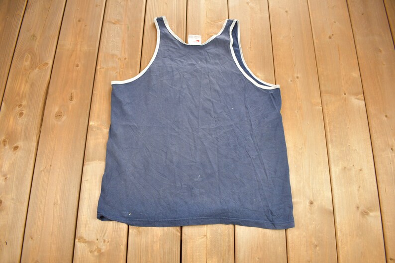 May include: A plain blue sleeveless shirt with a white trim around the neck and armholes.