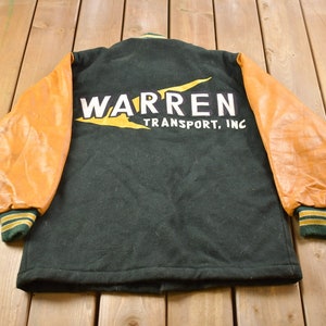 May include: A green and brown varsity jacket with leather sleeves. The back of the jacket has a yellow lightning bolt and the text "WARREN TRANSPORT, INC."