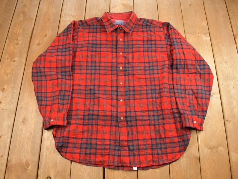 Puede incluir: Una camisa de manga larga a cuadros rojos y negros con cierre de botones.