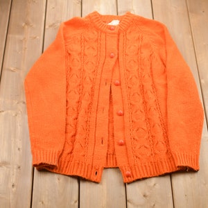 May include: Orange knitted cardigan with a cable knit pattern and button closure.
