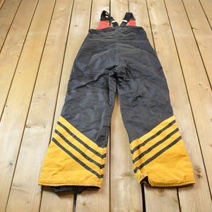 May include: Black ski overalls with yellow and black stripes on the legs. The straps are red and black.