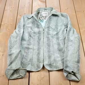 May include: A light blue denim jacket with a snakeskin pattern and a zip closure. The jacket has a collar and long sleeves.