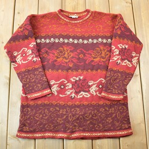 Peut inclure: Un pull à col rond avec un motif rouge, blanc et marron. Le pull a un motif floral.