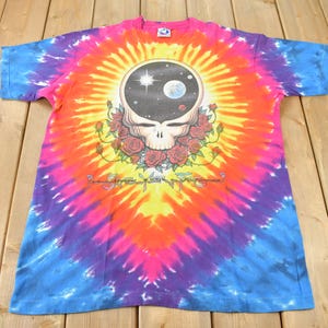 May include: Tie-dye t-shirt featuring a colorful swirl pattern with a Grateful Dead Steal Your Face logo in the center. The logo is surrounded by roses and a black background with stars and a planet.