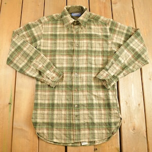 Può includere: Una camicia di flanella a quadri verde e marrone con maniche lunghe e chiusura con bottoni.