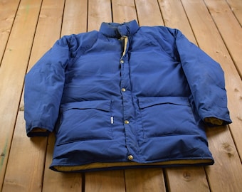 May include: A blue puffer jacket with a snap closure and two large pockets. The jacket has a brown lining.