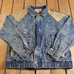 Könnte beinhalten: Eine blaue Jeansjacke mit einem verblassten, acid-gewaschenen Effekt. Die Jacke hat braune Lederakzente an den Schultern und einen Reißverschluss. Die Jacke hat einen Kordelzug am unteren Rand.
