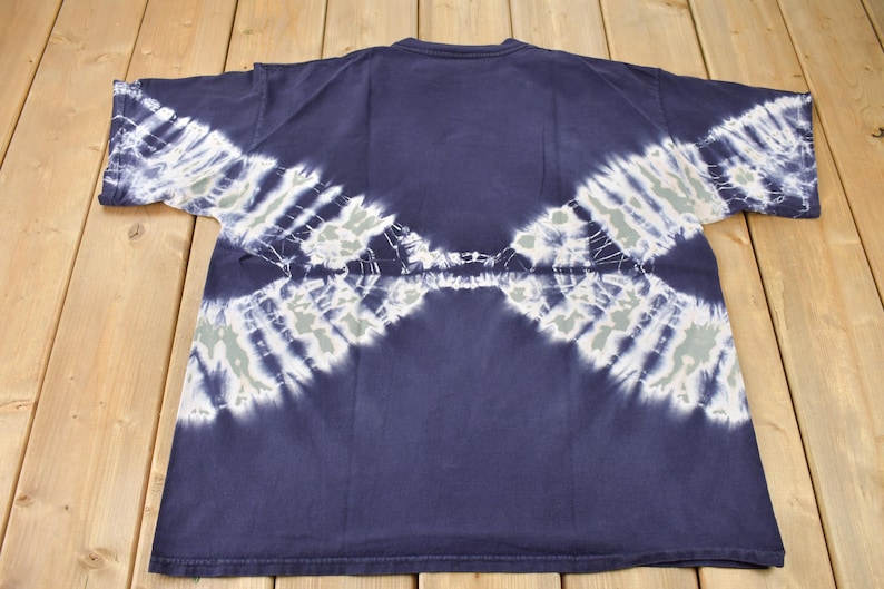 May include: A navy blue tie-dye t-shirt with white and light blue patterns. The shirt has a crew neck and short sleeves.